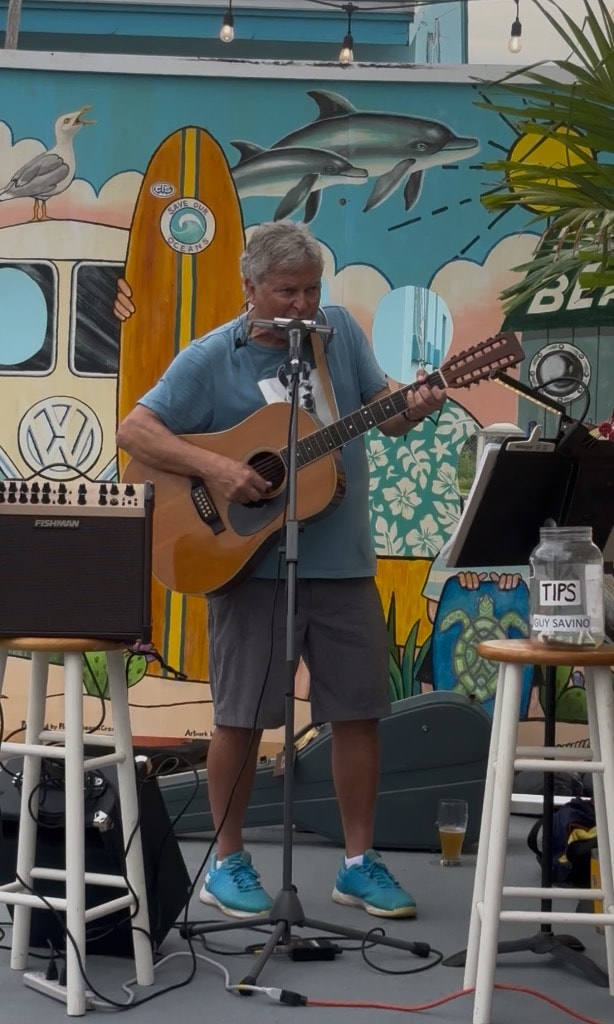 Guy Savino performing live with beach mural backdrop